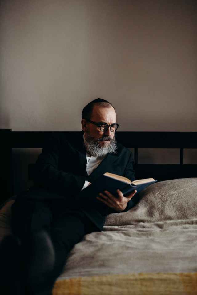 bearded man reading a book in bed