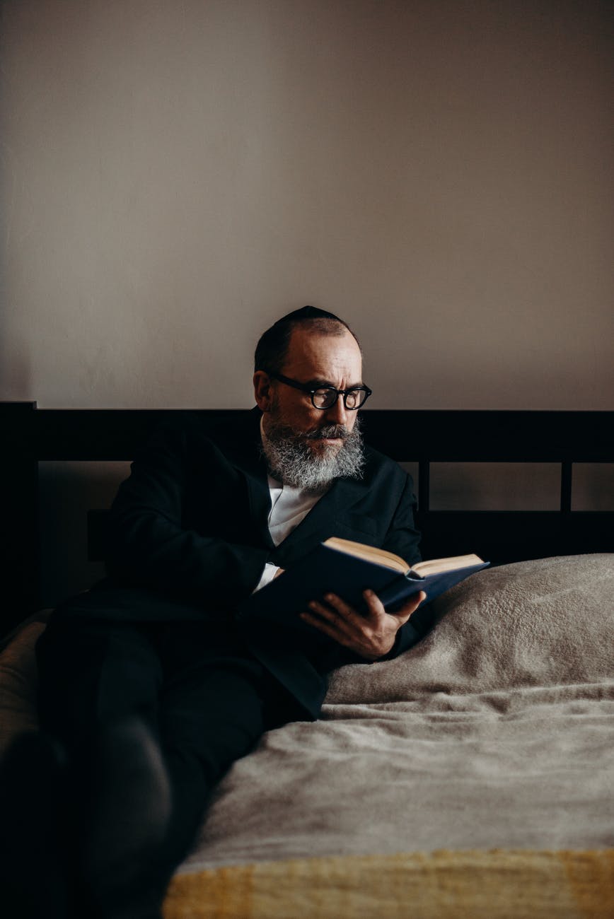 bearded man reading a book in bed