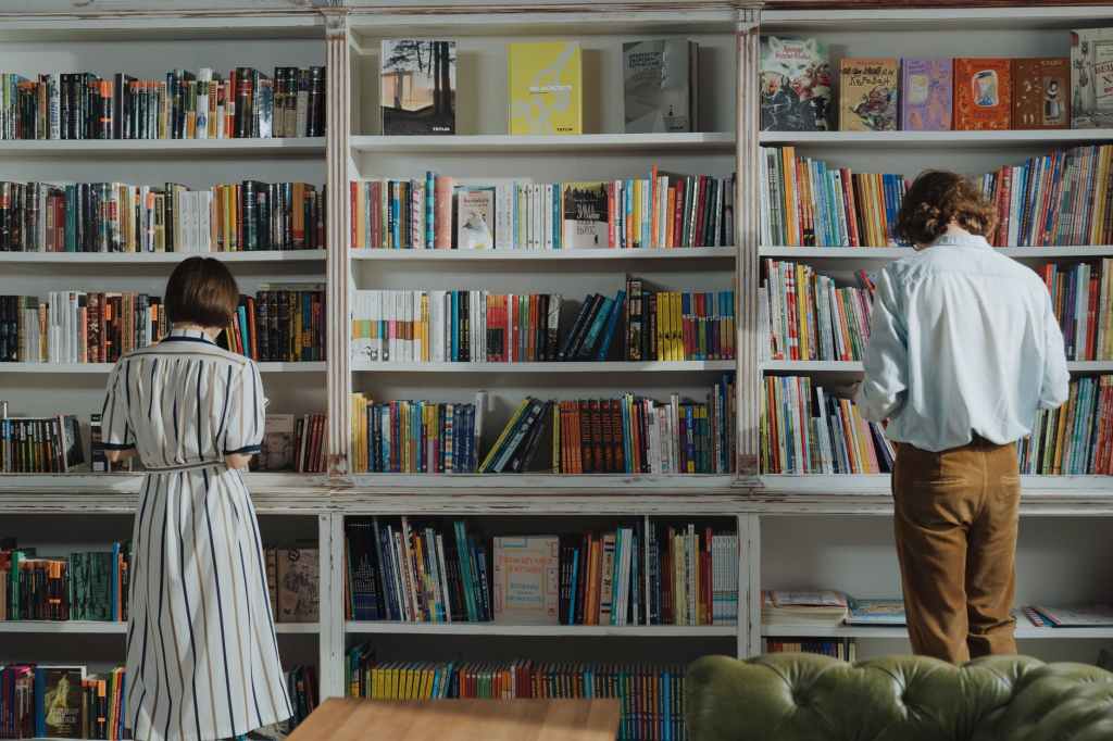 man in white dress shirt standing beside brown wooden book shelf