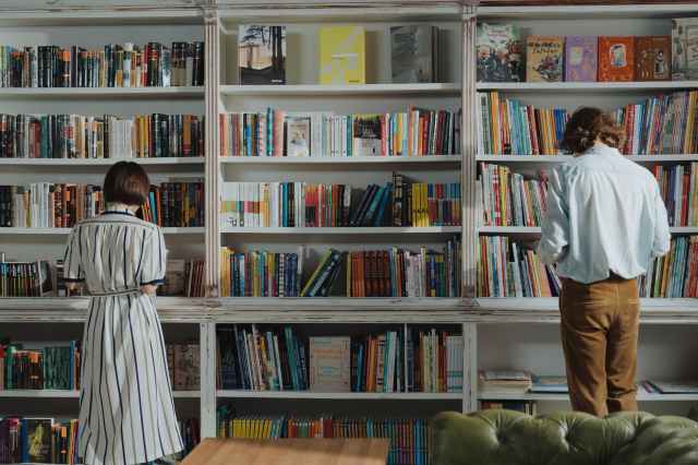 man in white dress shirt standing beside brown wooden book shelf